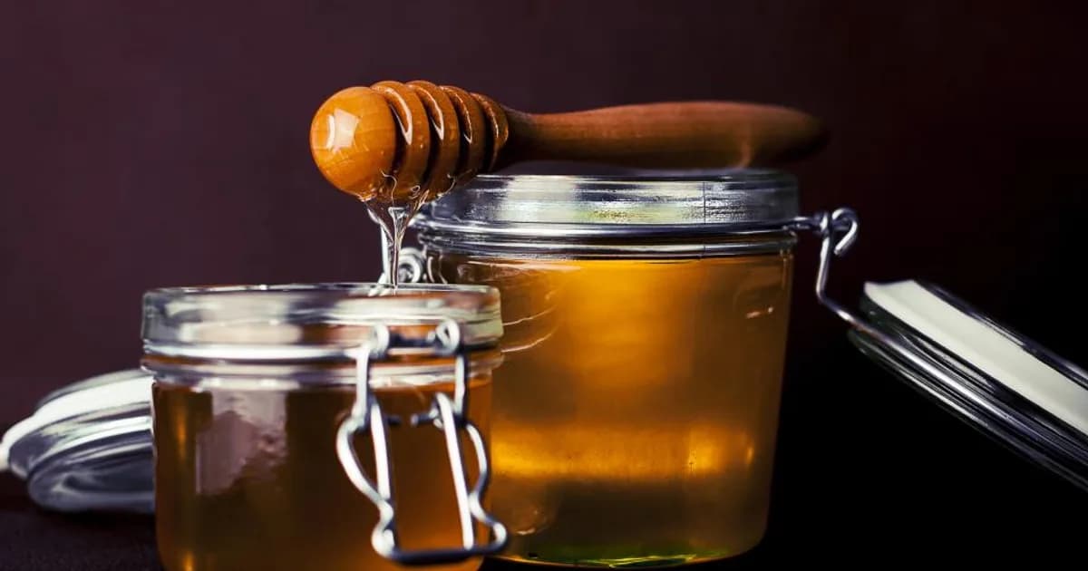Deux jares de miel en verre et une cuillère en bois, miel liquide et filant